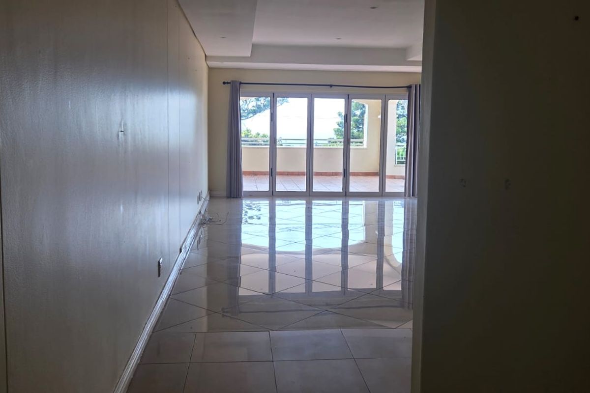 A spacious, empty living area featuring polished tiled floors, recessed lighting, and large sliding glass doors that open onto an outdoor balcony.