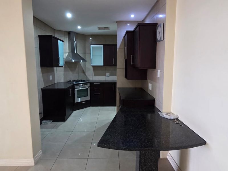 A modern kitchen featuring dark wood cabinetry, granite countertops, a breakfast bar, and built-in stainless steel appliances, set against neutral tiled flooring.