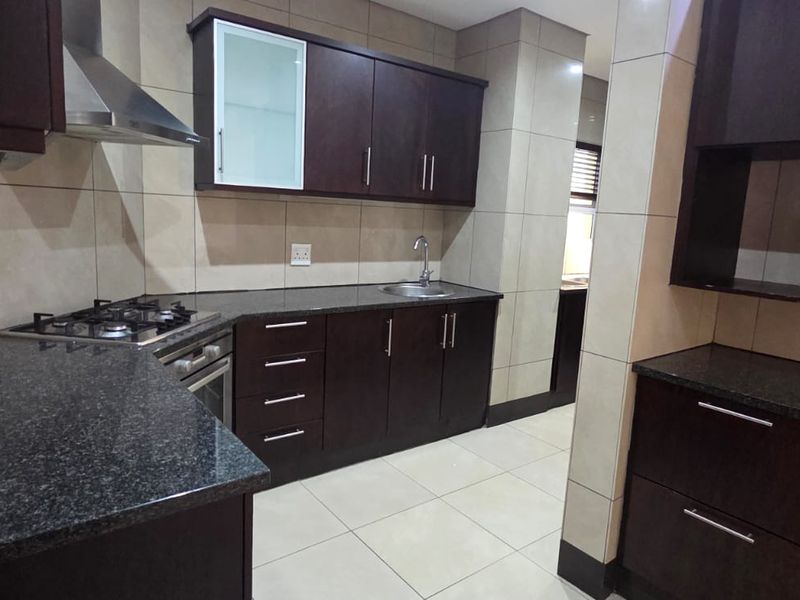 Modern kitchen featuring dark wood cabinetry, granite countertops, gas hob, extractor fan, and tiled finishes throughout.