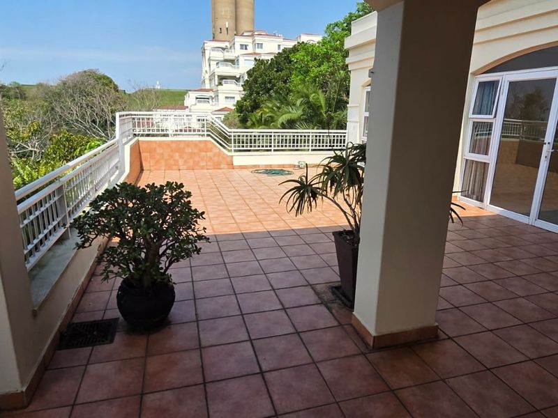 Spacious covered balcony featuring tiled flooring and metal balustrades, providing an open outdoor area accessible through large sliding glass doors.