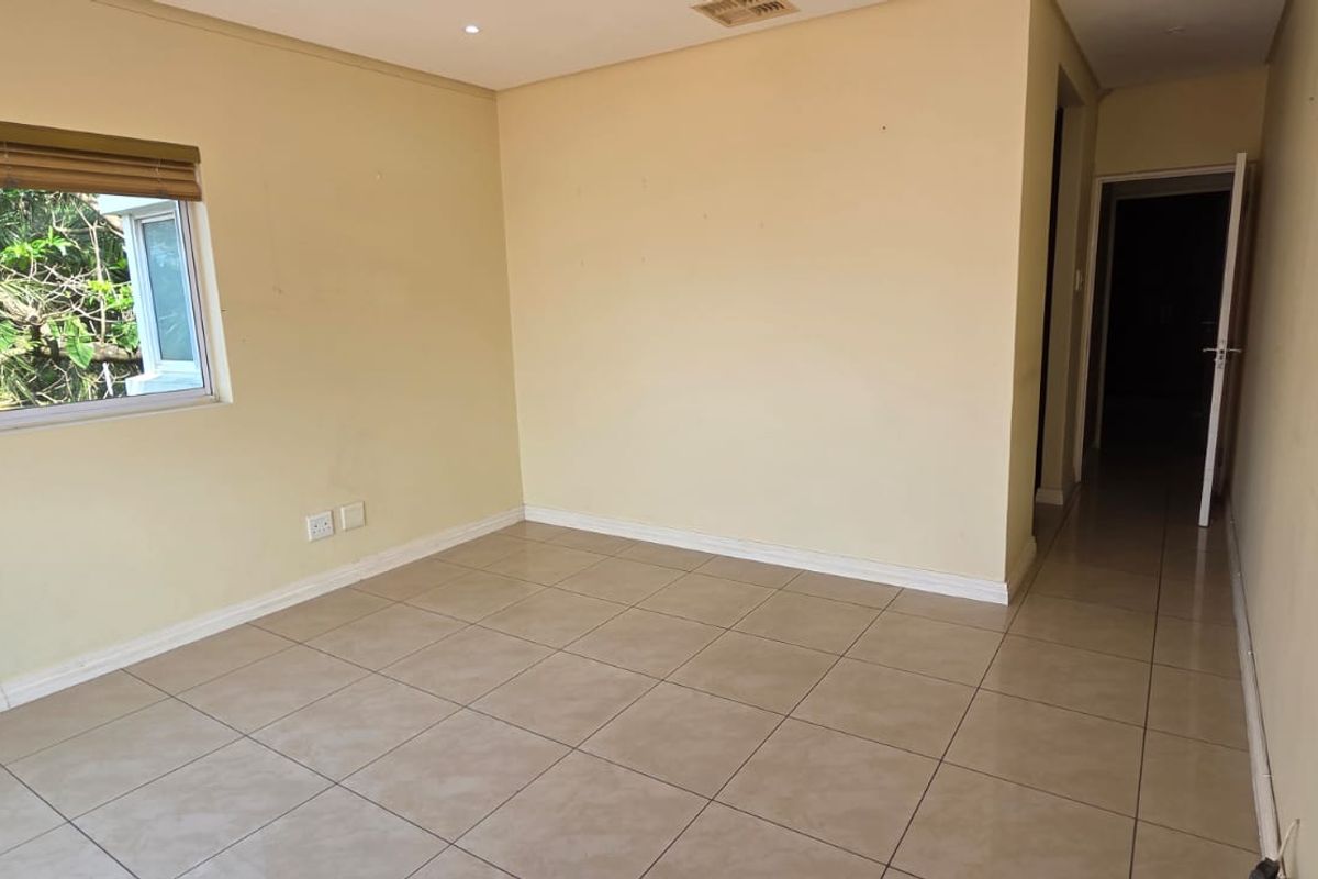 An empty bedroom featuring neutral tiled flooring, recessed lighting, and a sliding window with a view of surrounding greenery.
