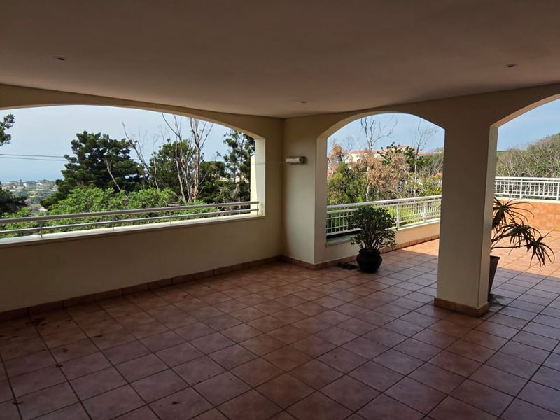 Spacious covered balcony featuring tiled flooring, arched architectural openings, and a metal balustrade with expansive outdoor views.