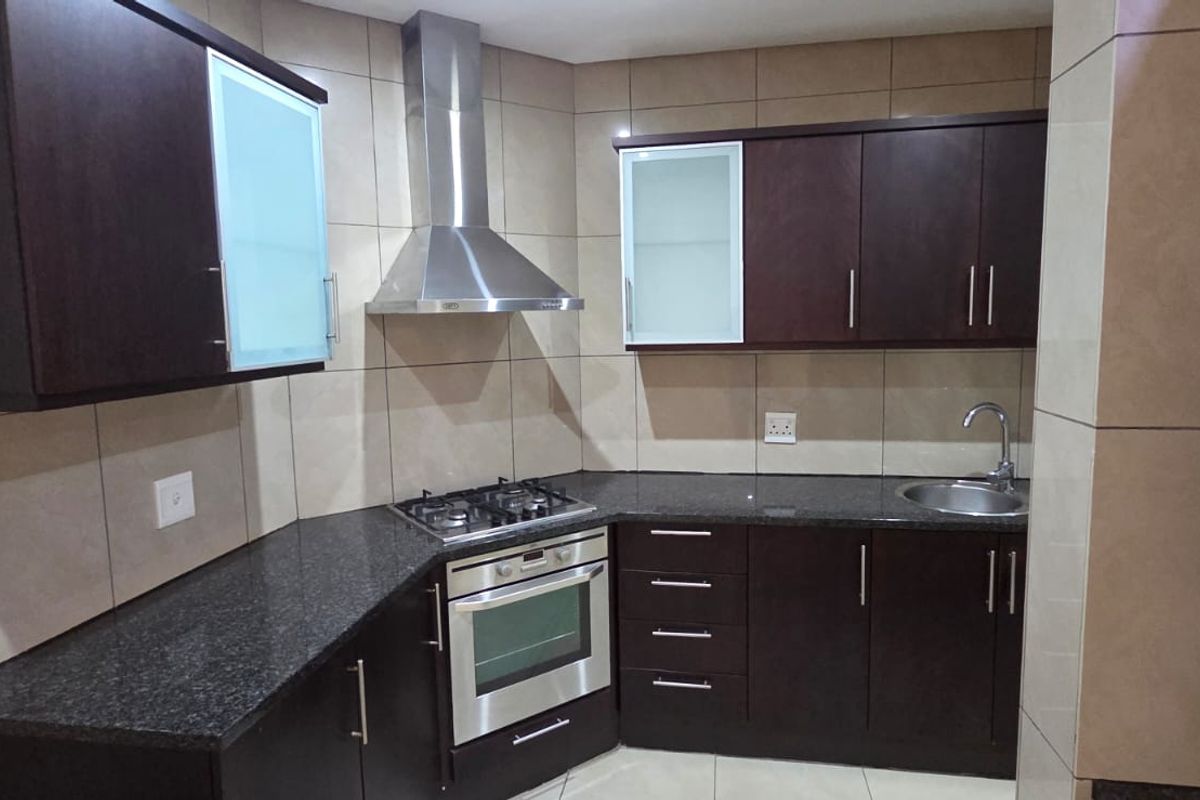 Modern kitchen featuring dark wood cabinetry, granite countertops, stainless steel appliances including a gas hob, oven, and extractor fan, with full-height wall tiling.