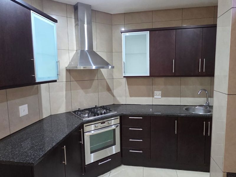 Modern kitchen featuring dark wood cabinetry, granite countertops, stainless steel appliances including a gas hob, oven, and extractor fan, with full-height wall tiling.