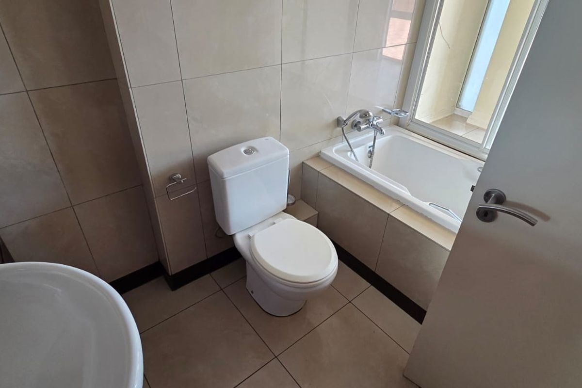 A clean, modern bathroom featuring a built-in bathtub, toilet, and basin with neutral wall and floor tiling.