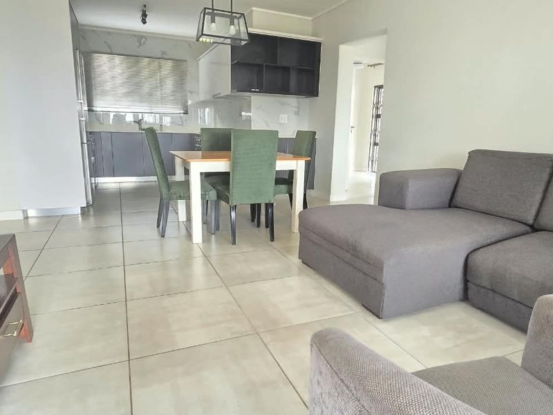 Open plan living and dining area featuring large format floor tiles and a modern kitchen with dark cabinetry.