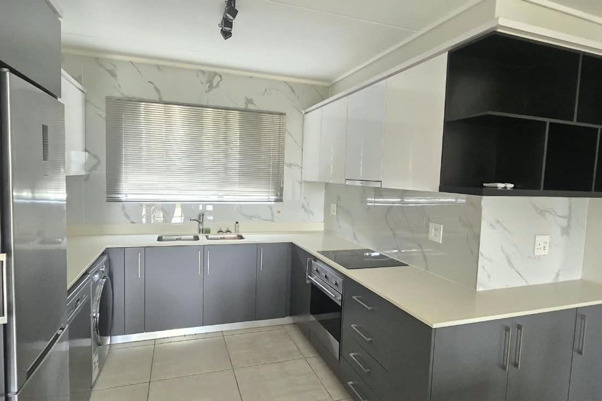 Modern kitchen featuring sleek grey and white cabinetry, stone countertops, marble-look splashback, and integrated appliances in a clean, contemporary layout.