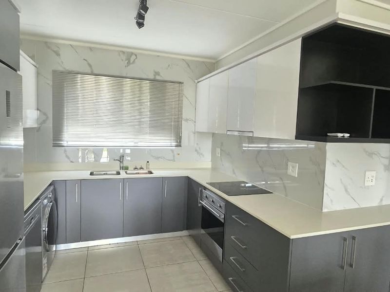 Modern kitchen featuring sleek grey and white cabinetry, stone countertops, marble-look splashback, and integrated appliances in a clean, contemporary layout.