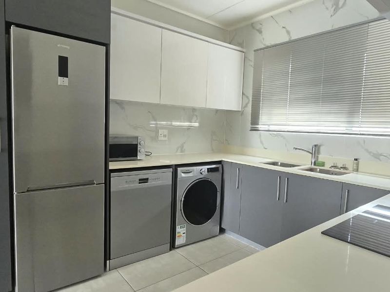 Modern kitchen featuring sleek grey and white cabinetry, stone countertops, marble-look splashback, and integrated stainless steel appliances.