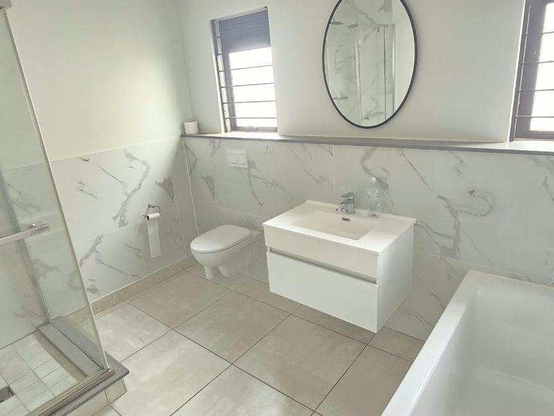 Modern bathroom featuring a walk-in shower, separate bathtub, wall-hung vanity, and wall-hung toilet, finished with elegant marble-look wall tiles.
