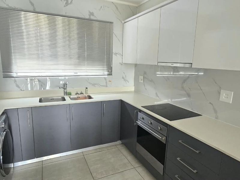Modern kitchen featuring sleek grey and white cabinetry, stone countertops, marble-look splashbacks, and integrated appliances including an oven and hob.