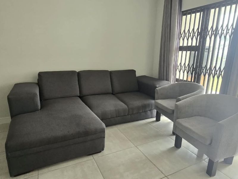 A bright living room featuring neutral tiled flooring and a large sliding glass door with an integrated security gate leading to the outdoors.