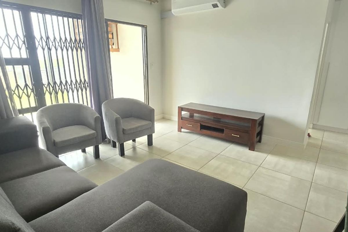 A bright living room featuring tiled flooring, a wall-mounted air conditioning unit, and a sliding door with a security gate leading to the exterior.