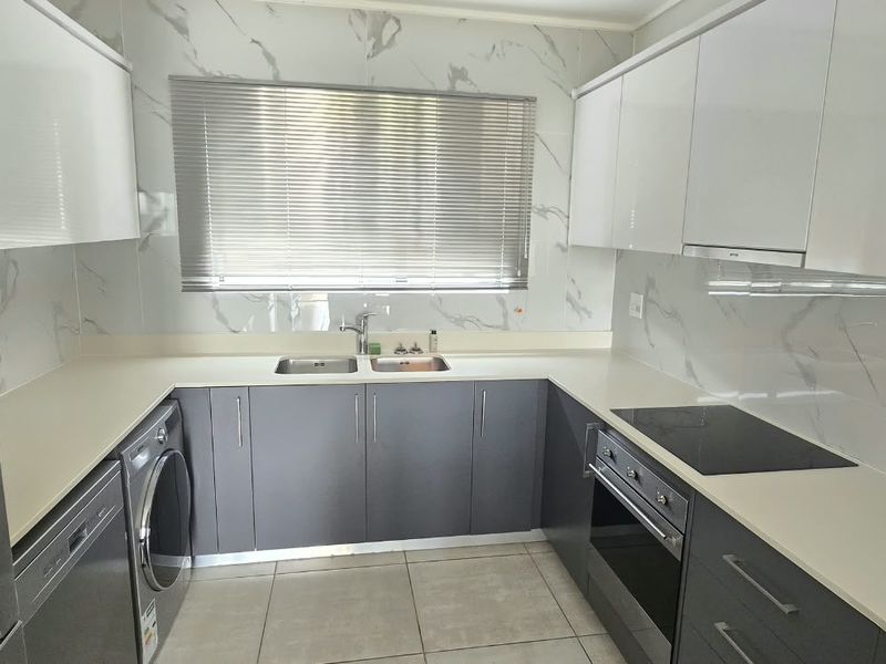 Modern kitchen featuring sleek grey and white cabinetry, stone countertops, marble-look splashbacks, and integrated appliances including an oven and hob.