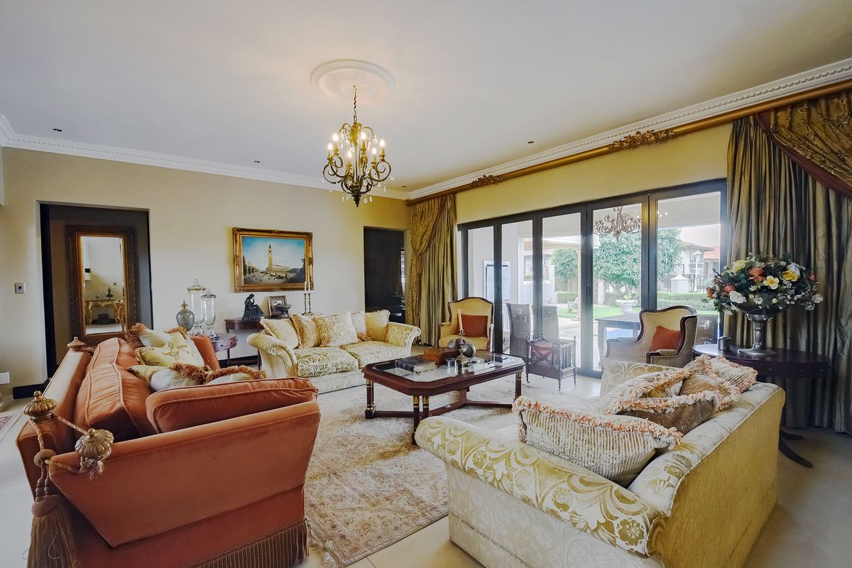 Spacious living room featuring elegant crown molding, a decorative ceiling rose with a chandelier, and large sliding glass doors providing access to the garden.
