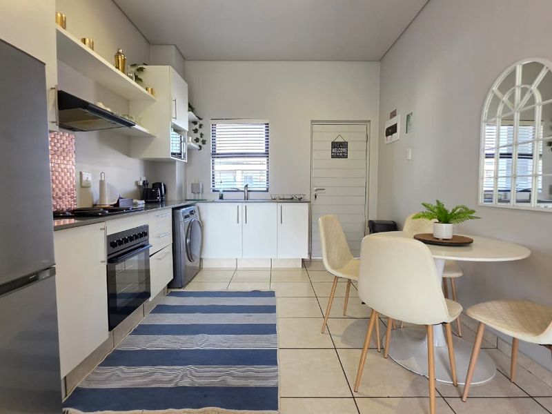 An open-plan kitchen and dining area featuring white cabinetry, built-in appliances, tiled flooring, and a functional layout suitable for modern apartment living.