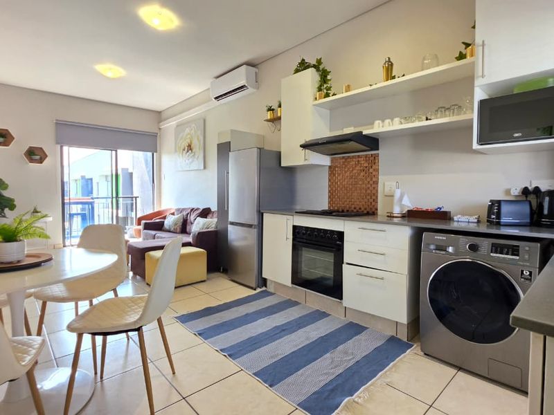 Open-plan living area featuring a modern kitchen with built-in appliances, tiled flooring, and direct access to a balcony through sliding doors.