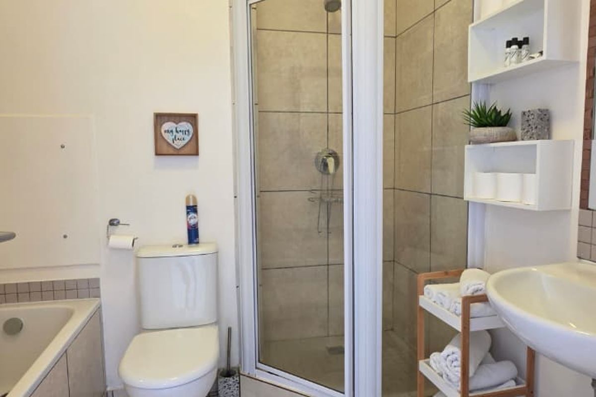 A functional bathroom featuring a separate shower enclosure, bathtub, pedestal basin, and neutral wall and floor tiling.