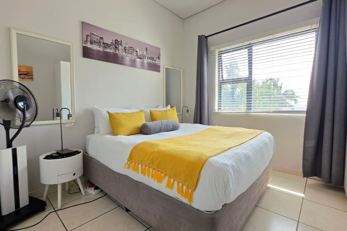 A well-lit bedroom featuring tiled flooring, a built-in wardrobe, and large windows with venetian blinds and curtains.