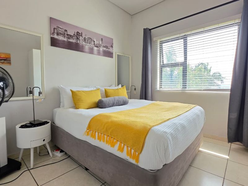 A well-lit bedroom featuring tiled flooring, a built-in wardrobe, and large windows with venetian blinds and curtains.