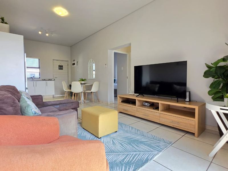 An open-plan living and dining area featuring tiled flooring and a compact kitchen space in the background.