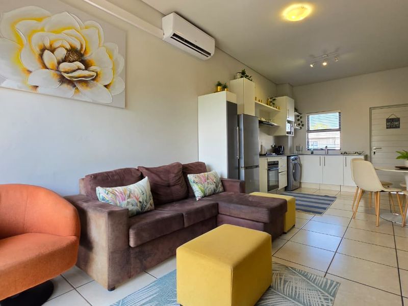 Open-plan living area featuring tiled floors, a compact kitchen with built-in cabinetry and appliances, and a wall-mounted air conditioning unit.