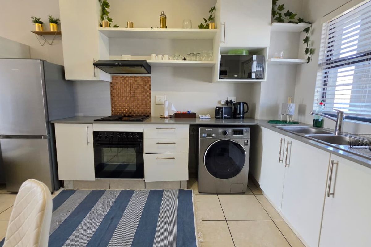 A functional kitchen featuring white cabinetry, built-in oven and hob, stainless steel sink, and tiled flooring with natural light from the window.
