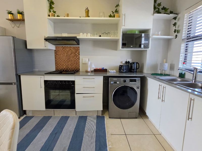 A functional kitchen featuring white cabinetry, built-in oven and hob, stainless steel sink, and tiled flooring with natural light from the window.
