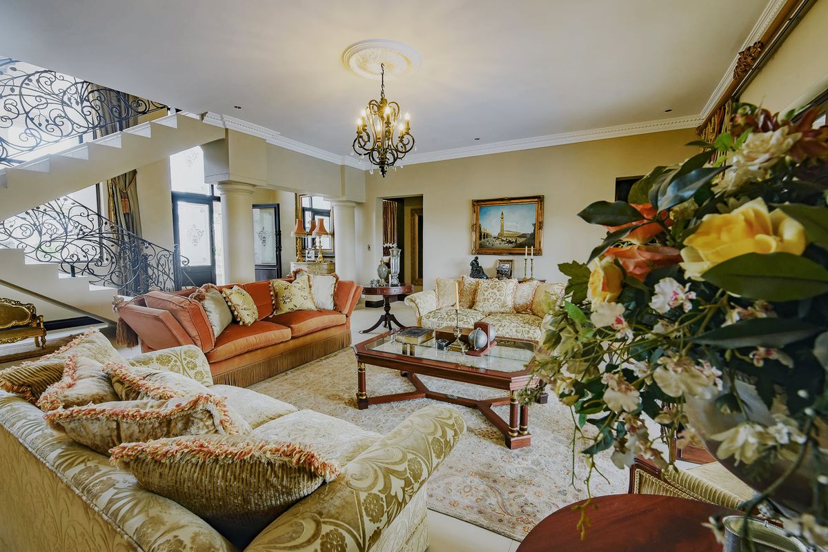 Spacious living room featuring a grand wrought iron staircase, decorative ceiling rose, and classic chandelier, creating an elegant and traditional atmosphere.