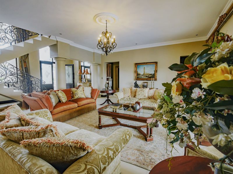Spacious living room featuring a grand wrought iron staircase, decorative ceiling rose, and classic chandelier, creating an elegant and traditional atmosphere.