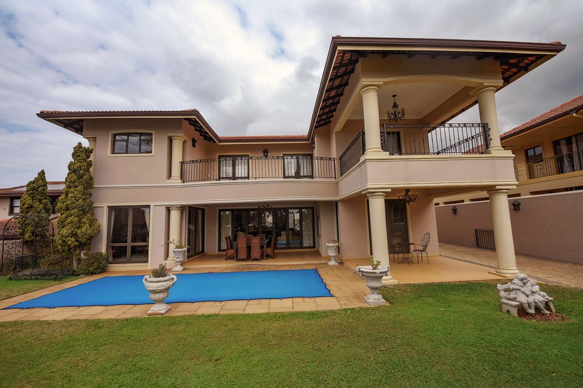 Rear view of a two-story house featuring a covered patio, upper-level balcony with wrought iron railings, and a swimming pool with a paved surround.