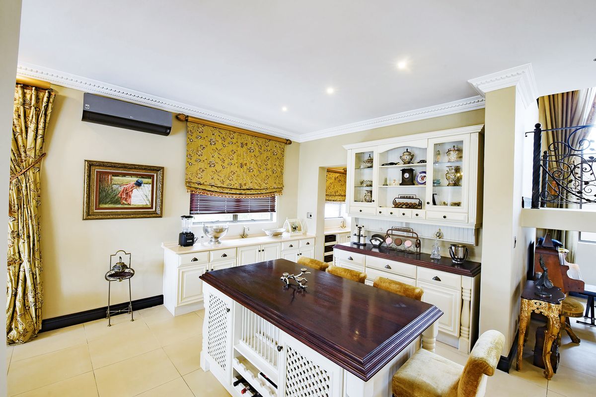 A well-maintained kitchen featuring classic white cabinetry, a dark wood-topped island, tiled flooring, and integrated air conditioning.