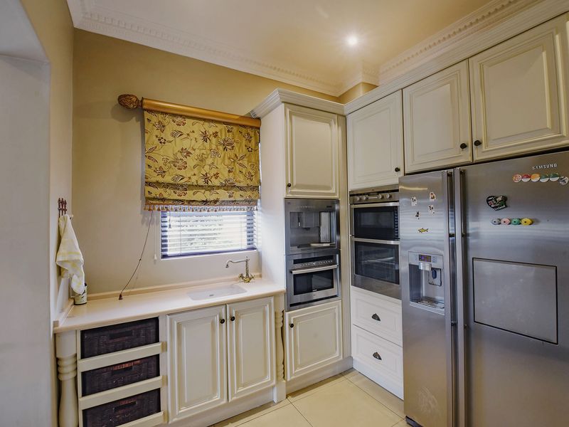 A well-appointed kitchen featuring classic cream cabinetry, integrated appliances including a double oven and coffee machine, and a functional prep sink area.