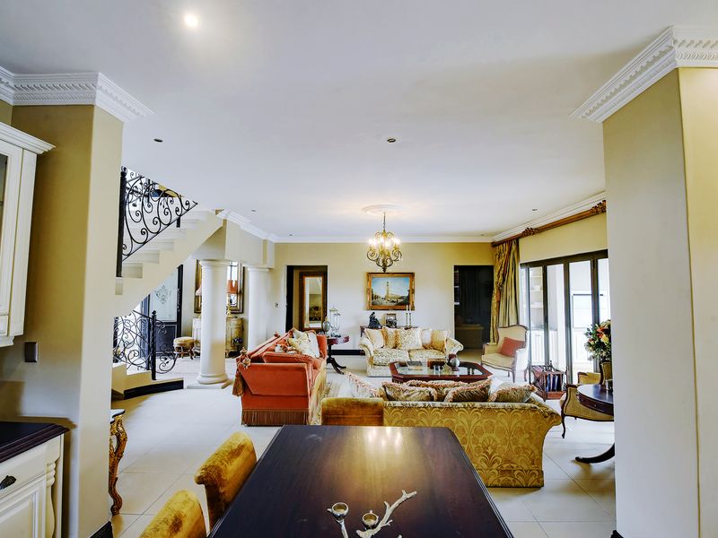 Spacious open-plan living area featuring tiled floors, decorative crown molding, a grand staircase with wrought iron railings, and direct access to outdoor space.