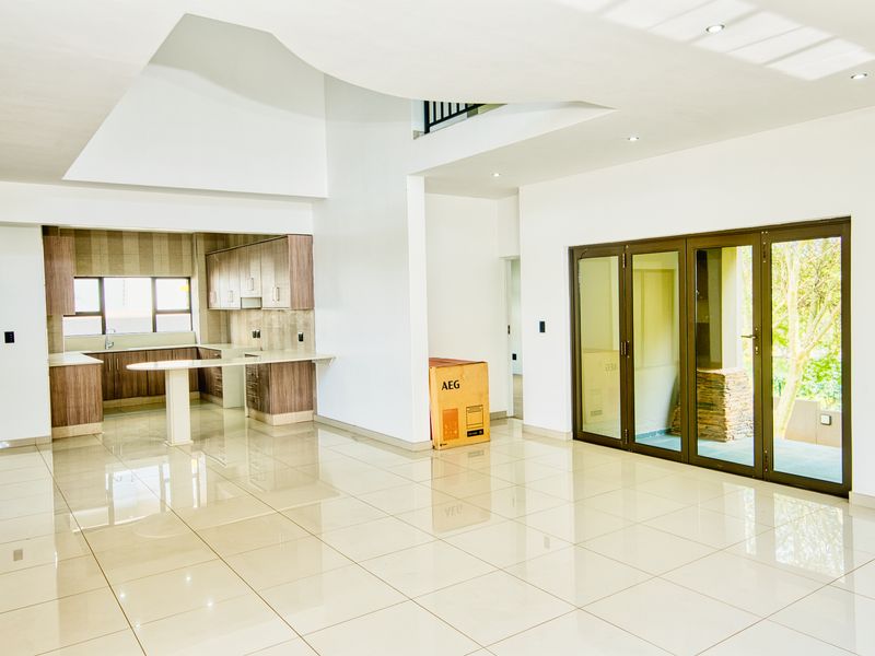 Spacious open-plan living area featuring high ceilings, large bi-fold doors leading to the outdoors, and a modern kitchen with built-in cabinetry and island.