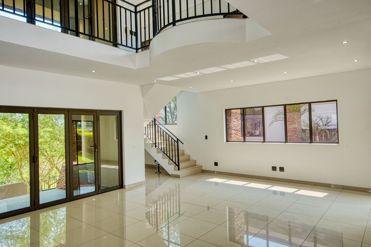 Spacious open-plan living area featuring high ceilings, a mezzanine level, tiled flooring, and large aluminium-framed windows and doors providing ample natural light.
