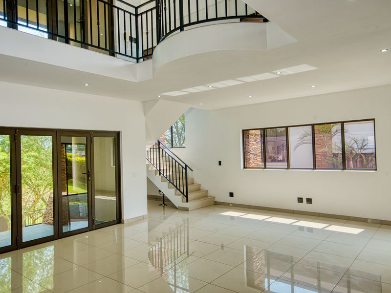 Spacious open-plan living area featuring high ceilings, a mezzanine level, tiled flooring, and large aluminium-framed windows and doors providing ample natural light.