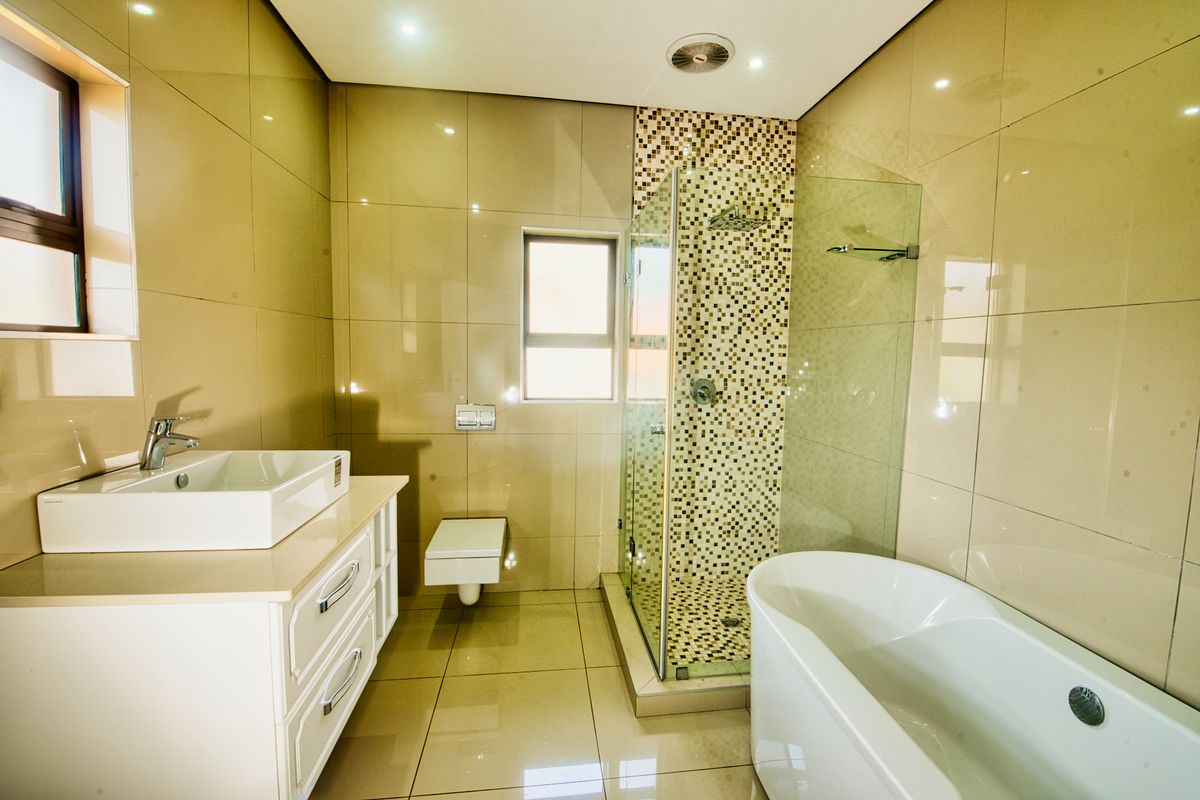 Modern bathroom featuring a wall-mounted toilet, vessel sink vanity, glass-enclosed shower with mosaic accents, and a sleek freestanding bathtub.