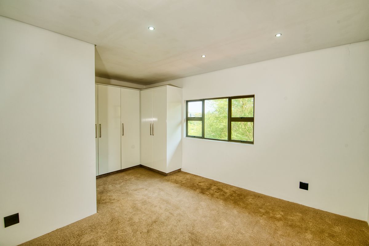 A bright, empty bedroom featuring neutral carpeting, built-in white cupboards, and recessed ceiling lighting.