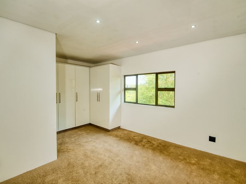 A bright, empty bedroom featuring neutral carpeting, built-in white cupboards, and recessed ceiling lighting.
