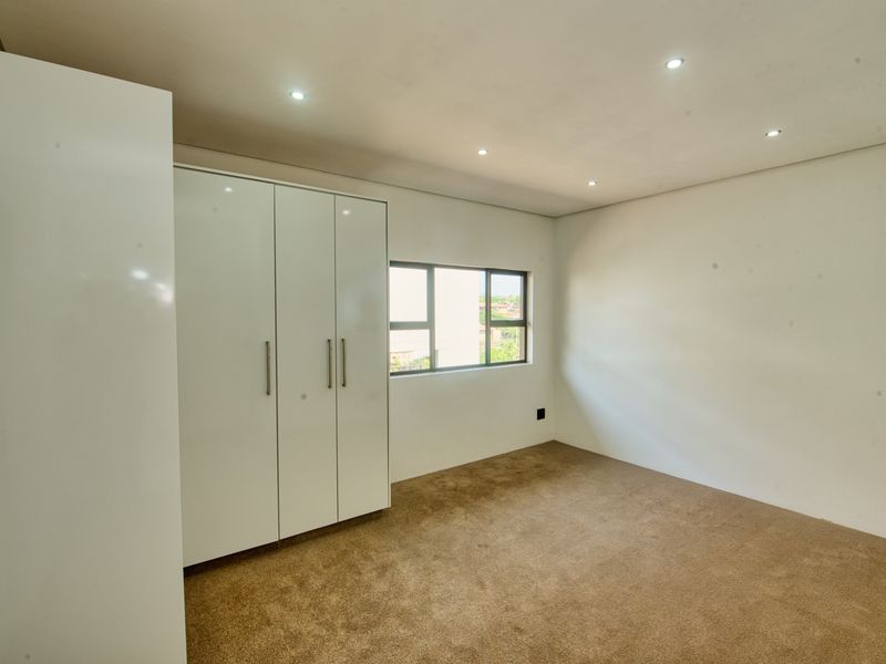 A clean, empty bedroom featuring built-in cupboards, recessed downlighting, and neutral carpeting, offering a blank canvas for personalization.