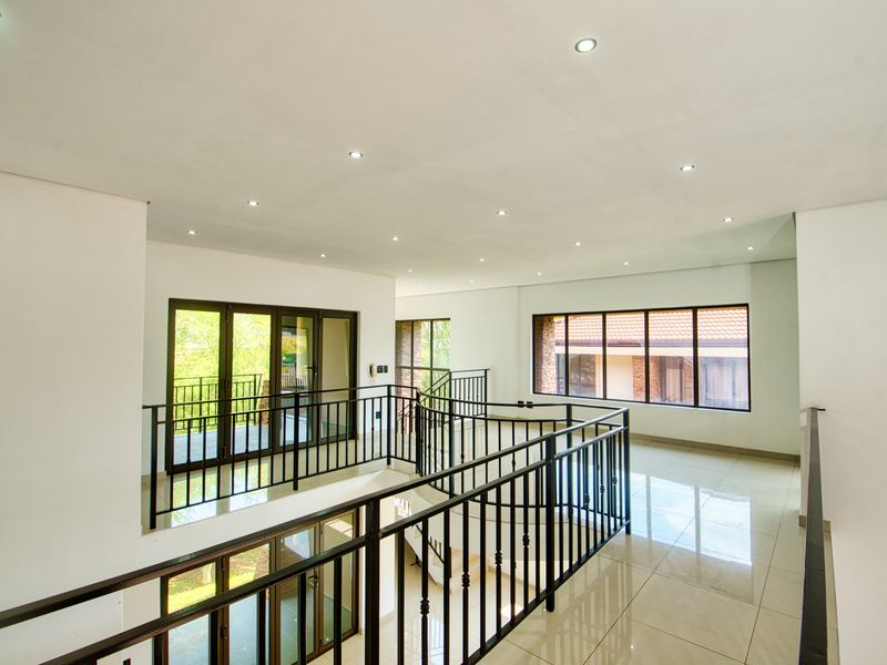 Spacious upper-level landing area featuring tiled flooring, modern recessed lighting, and a secure wrought iron balustrade overlooking the lower level.