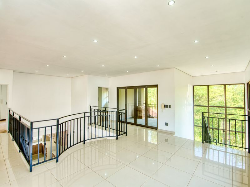 Spacious, light-filled landing area featuring polished porcelain tiles, a decorative wrought iron balustrade, and large windows overlooking the surrounding greenery.