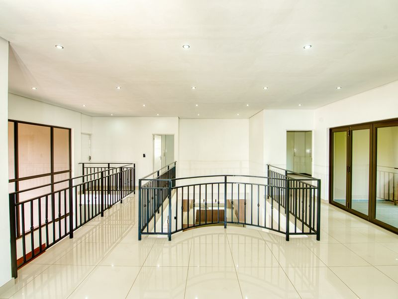 Spacious upper-level landing or hallway featuring polished porcelain floor tiles, modern recessed lighting, and a decorative wrought iron balustrade overlooking the lower level.