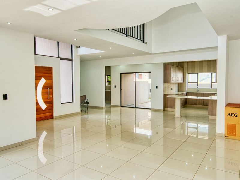 Spacious open-plan living area featuring high ceilings, tiled floors, a modern kitchen with cabinetry, and a mezzanine level overlooking the entrance.