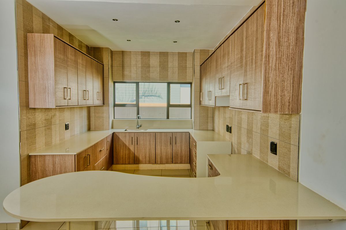 A clean, modern kitchen featuring wood-finish cabinetry, stone countertops, and a functional U-shaped layout with ample storage space.