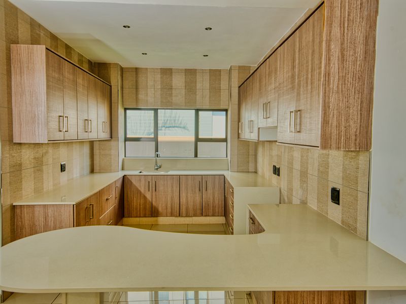 A clean, modern kitchen featuring wood-finish cabinetry, stone countertops, and a functional U-shaped layout with ample storage space.