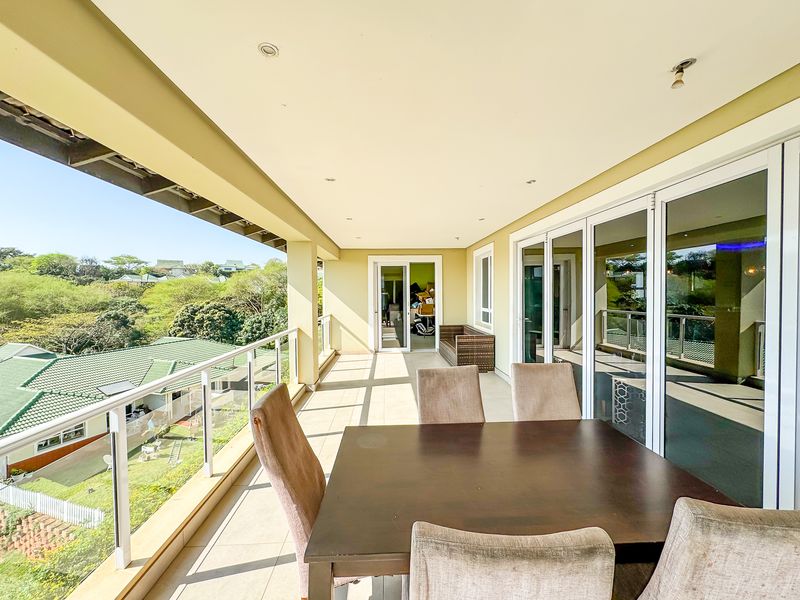 Spacious covered balcony featuring tiled flooring, glass balustrades, and large sliding doors, offering an elevated view of the surrounding neighborhood.