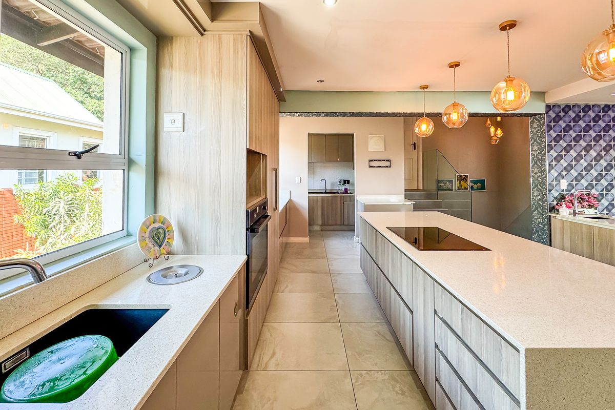 Modern kitchen featuring sleek cabinetry, stone countertops, a central island with an induction hob, and an adjacent scullery area with high-quality finishes.