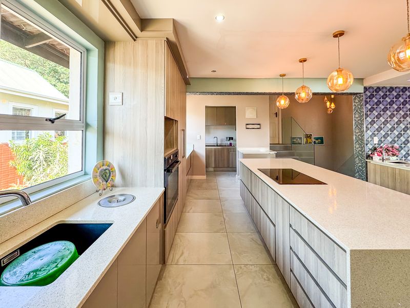 Modern kitchen featuring sleek cabinetry, stone countertops, a central island with an induction hob, and an adjacent scullery area with high-quality finishes.